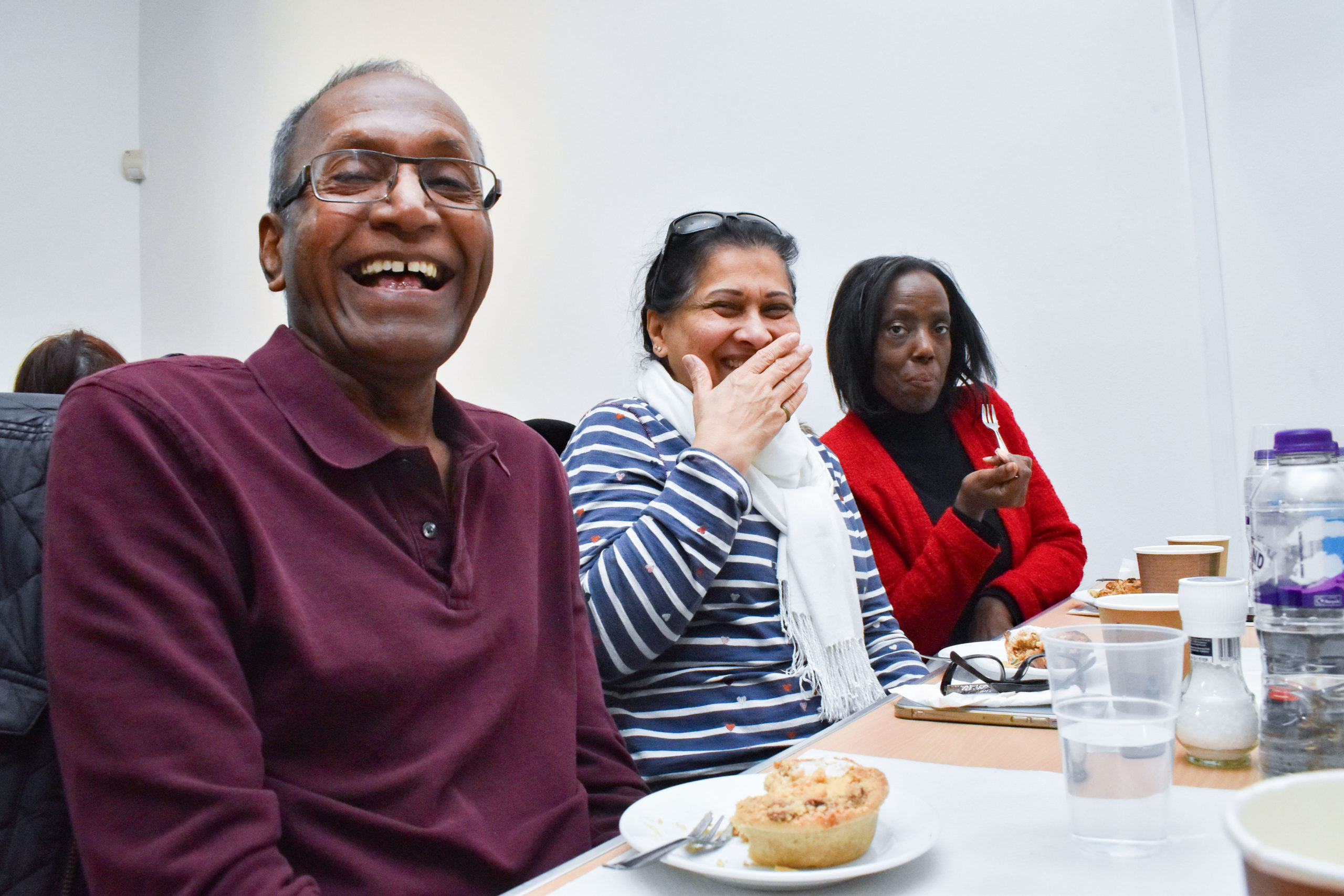 A man and two women are laughing while enjoying the lunch club.