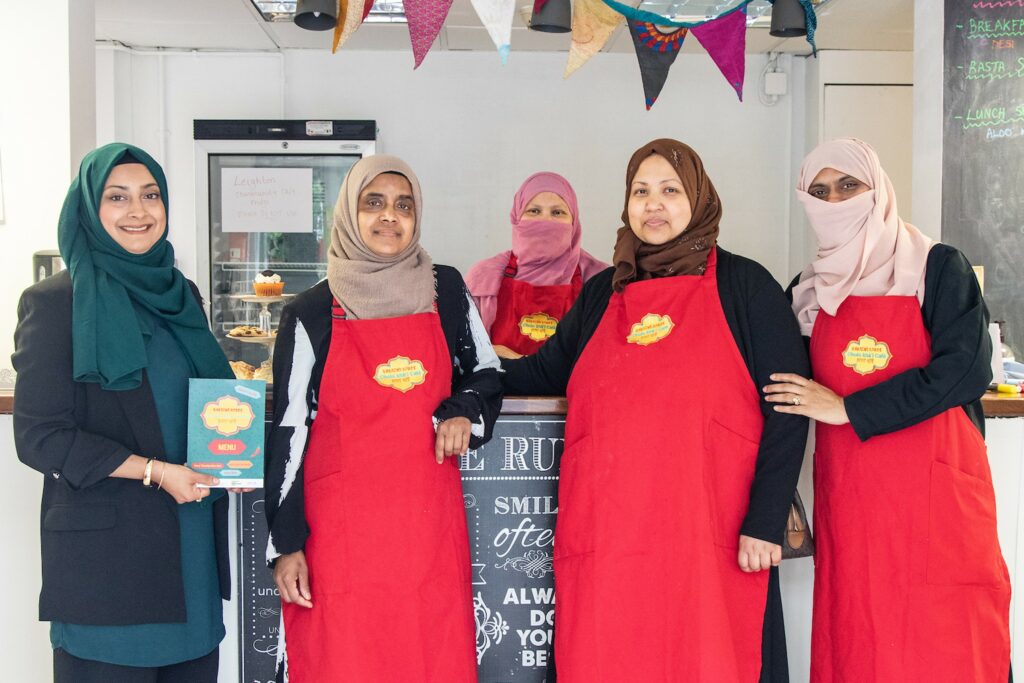 Five women involved in running the café stand around the café counter smiling at the camera.