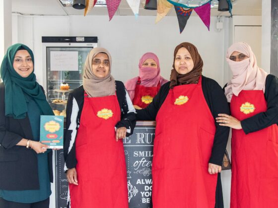 Five women involved in running the café stand around the café counter smiling at the camera.