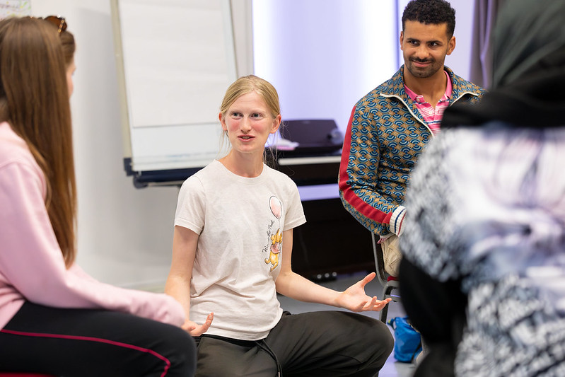 Nell is in the centre of the photo, sitting down cross legged and talking to the group. There are three participants either side of her.