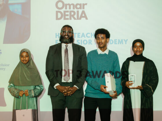 Abdiwahab Ali stands on stage, in line with three young people holding their awards, smiling at the camera.